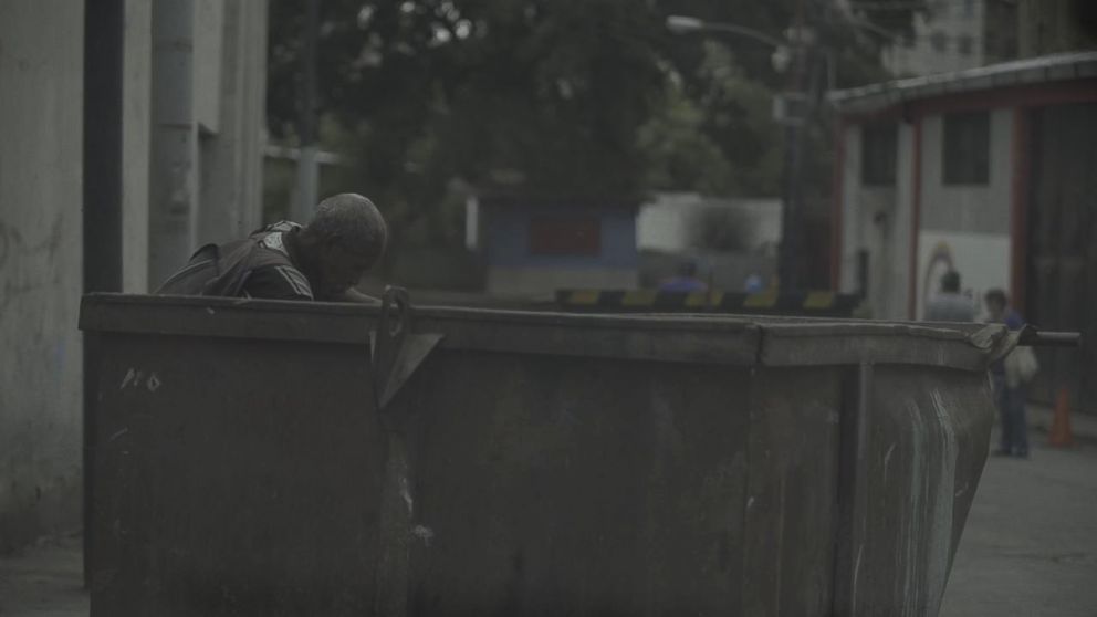 PHOTO: A man eats searches a trash container for food in Caracas, Venezuela. Food shortages and soaring inflation has forced many to rummage for food.