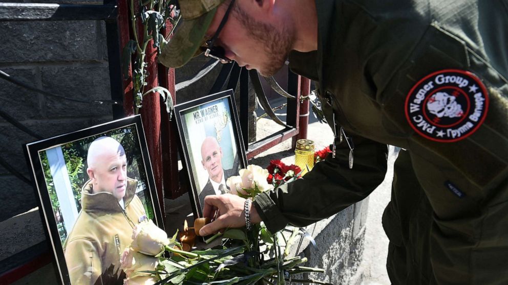 PHOTO: TOPSHOT - A member of private mercenary group Wagner pays tribute to Yevgeny Prigozhin (L) and Dmitry Utkin at the makeshift memorial in front of the PMC Wagner office in Novosibirsk, on August 24, 2023.