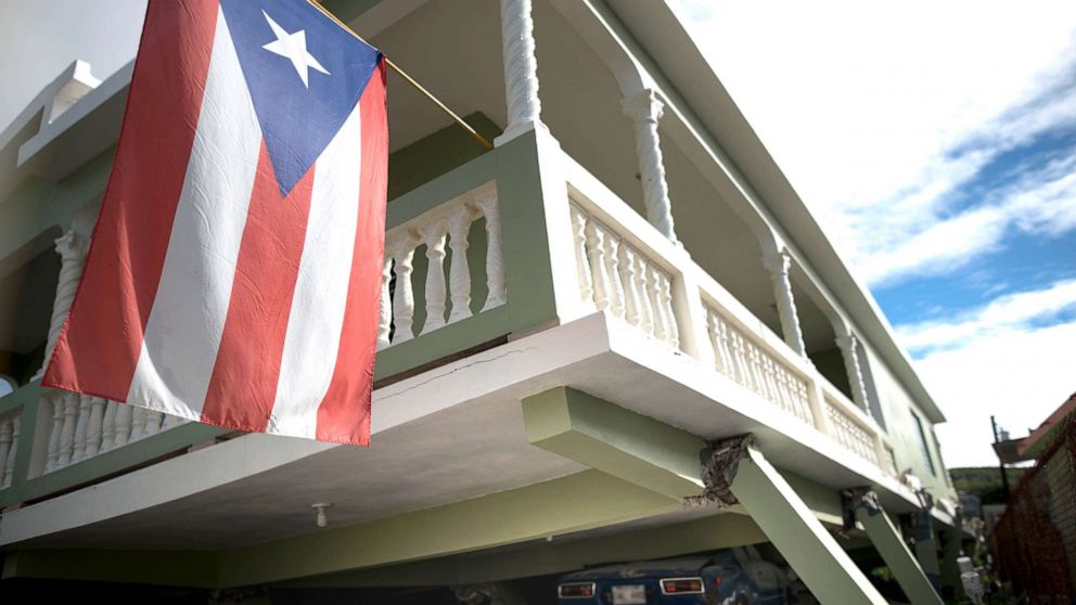 PHOTO: A Puerto Rican flag hangs from the porch of a home that collapsed on top of parked cars after an earthquake hit Guanica, Puerto Rico, Jan. 6, 2020.