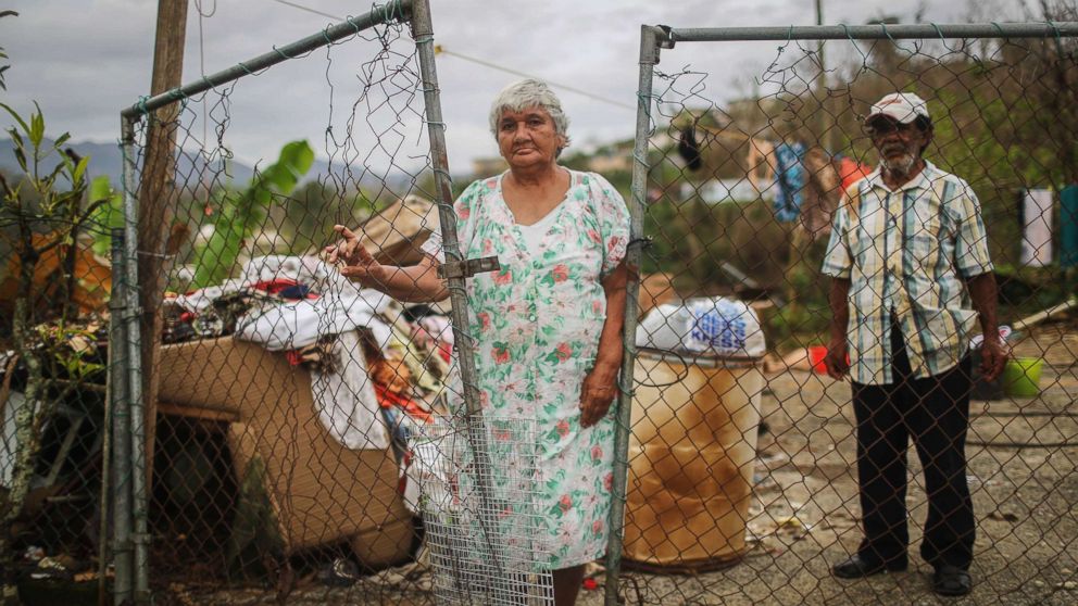PHOTO: Luz Sota Rivera (C) and Francisco Nazario Aviles pose outside their damaged home, with debris removed from their home uncollected in the driveway, three weeks after Hurricane Maria hit the island, Oct. 12, 2017 in Jayuya, Puerto Rico.