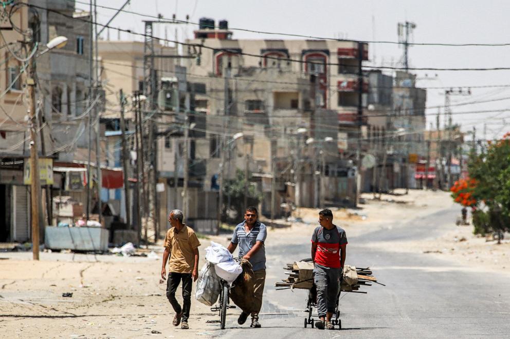 PHOTO: A man pulls a cart loaded with salvaged wood alongside another pushing a bicycle loaded with bags along a street in the eastern part of Rafah in the southern Gaza Strip on June 14, 2024.