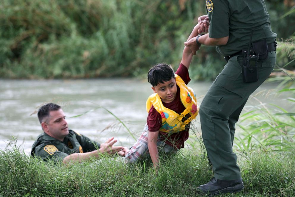 PHOTO: Border Patrol Agent in Charge Eagle Pass, Bryan Kemmett, left, passes a 7-year-old boy from Honduras to another agent after he was rescued from the swollen Rio Grande River, near Eagle Pass, Texas, May 10. 2019.