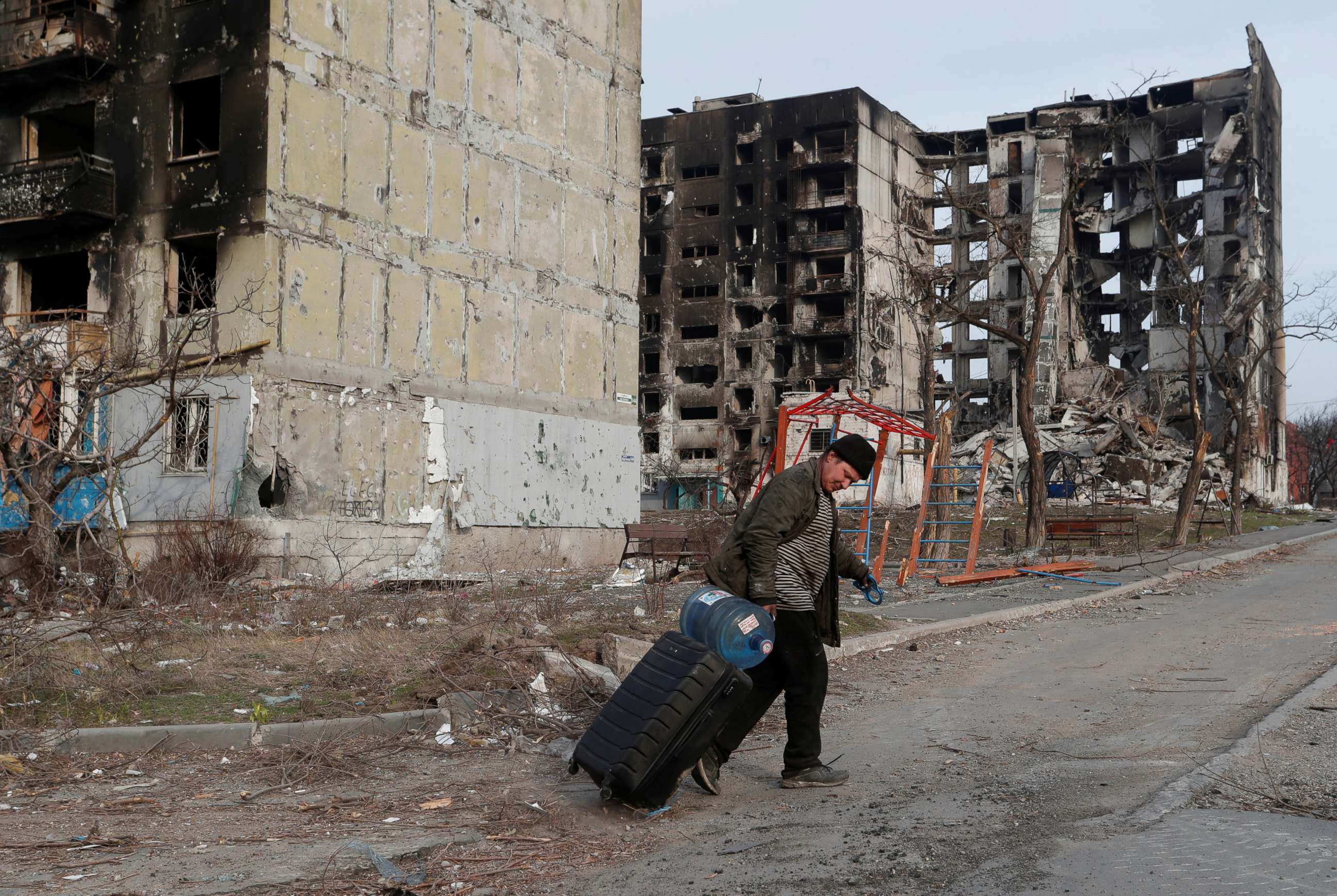 PHOTO: A local resident walks with a suitcase past destroyed apartment buildings in the besieged southern port city of Mariupol, Ukraine, on March 30, 2022, amid Russia's invasion of Ukraine.
