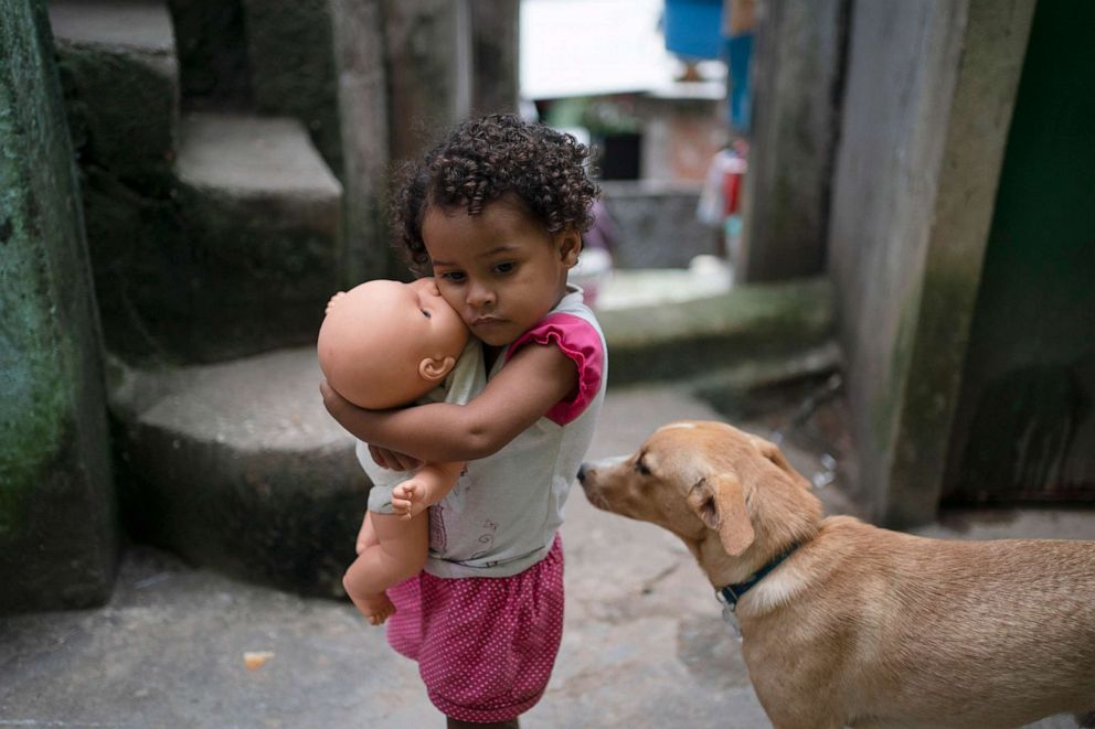 PHOTO: A girl holds her doll in an alley of the Rocinha slum of Rio de Janeiro, Brazil, March 24, 2020. The narrow alleyways of the country's largest favela reduce airflow around homes packed tightly together.