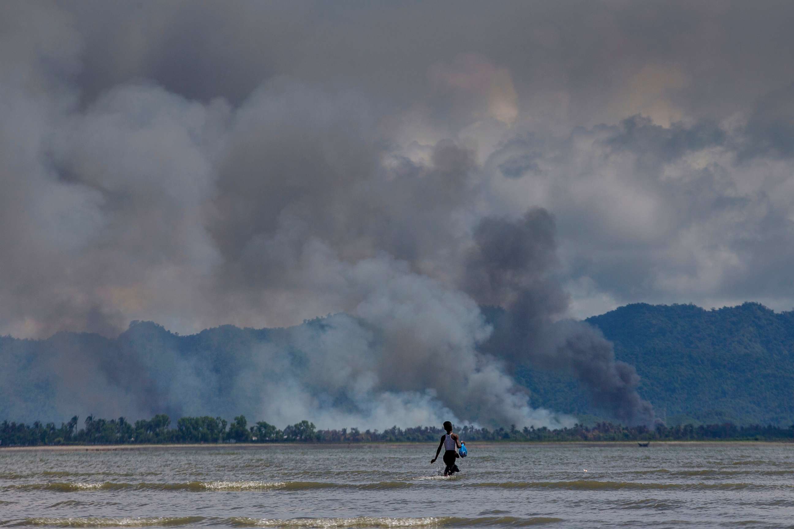 PHOTO: A Bangladeshi boy walks towards a parked boat as smoke rises from across the border in Myanmar, at Shah Porir Dwip, Bangladesh, Sept. 14, 2017. 