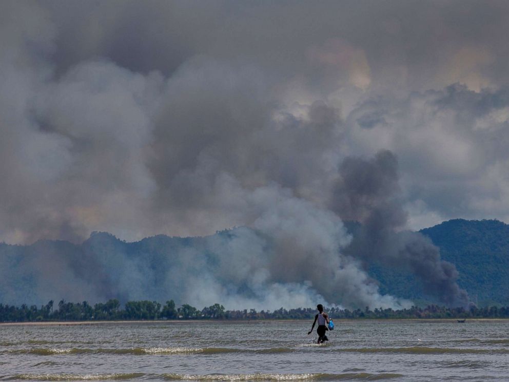 PHOTO: A Bangladeshi boy walks towards a parked boat as smoke rises from across the border in Myanmar, at Shah Porir Dwip, Bangladesh, Sept. 14, 2017.