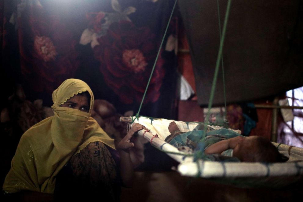 PHOTO: In this Tuesday, June 26, 2018, photo, "M" sits in her shelter, rocking her baby boy who had awoken from his sleep, in Kutupalong refugee camp in Bangladesh.