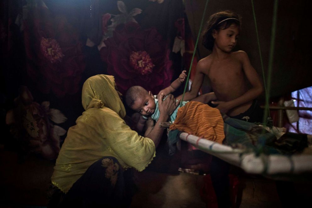 PHOTO: M's daughter, right, hands over her brother to their mother in their shelter in Kutupalong refugee camp in Bangladesh. "M" was raped by six soldiers from Myanmar's security forces after they strangled her 2-year-old son to death,  June 26, 2018.