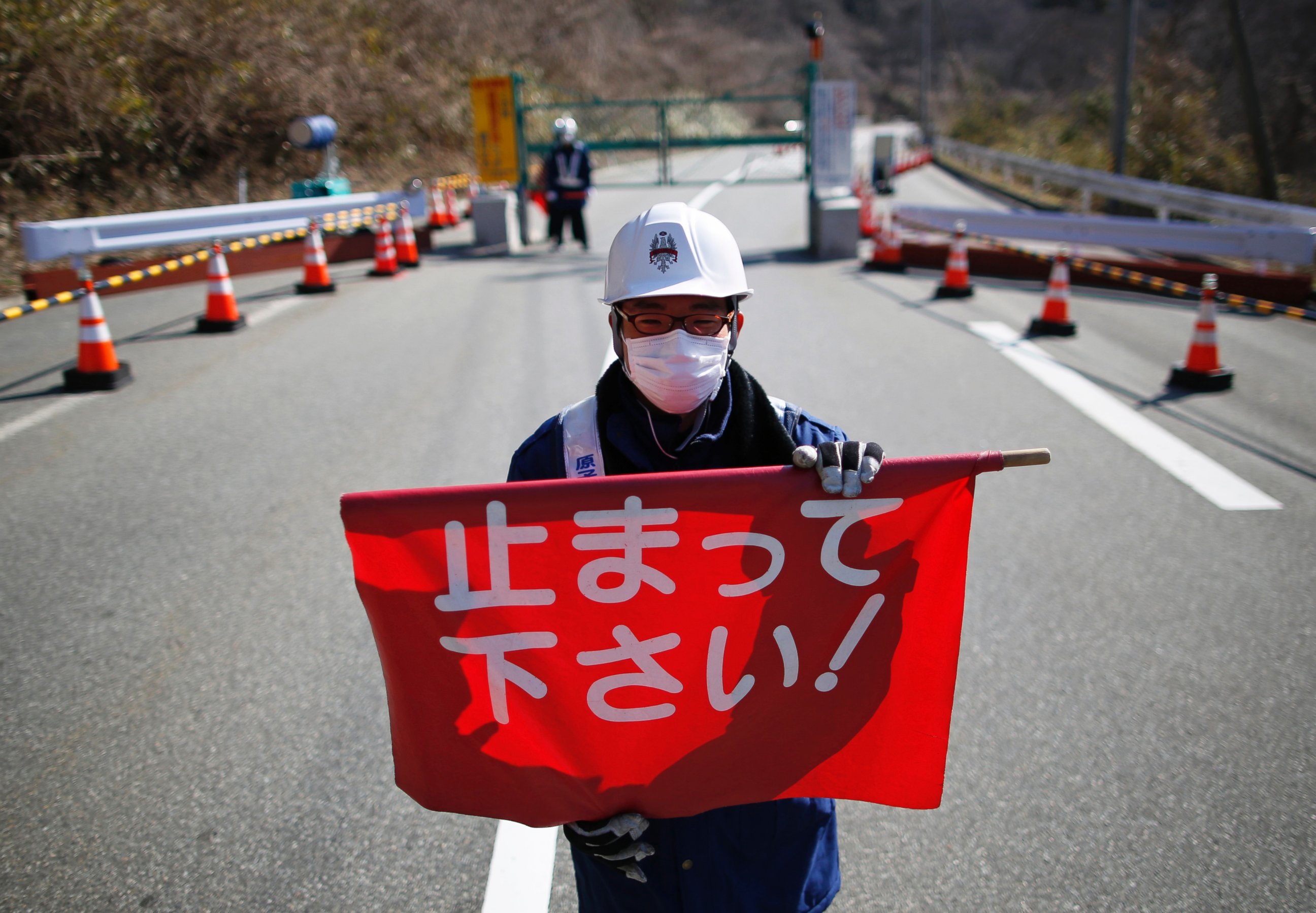 PHOTO: A security guard holds a flag, which reads "Please Stop!", as he stand by a steel gate at the border near Fukushima