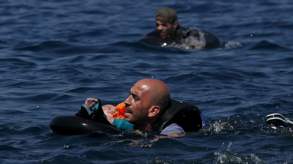 PHOTO: A Syrian refugee holds a baby in a flotation device as he swims towards the shore after their dinghy deflated before reaching the Greek island of Lesbos, Sept. 13, 2015.