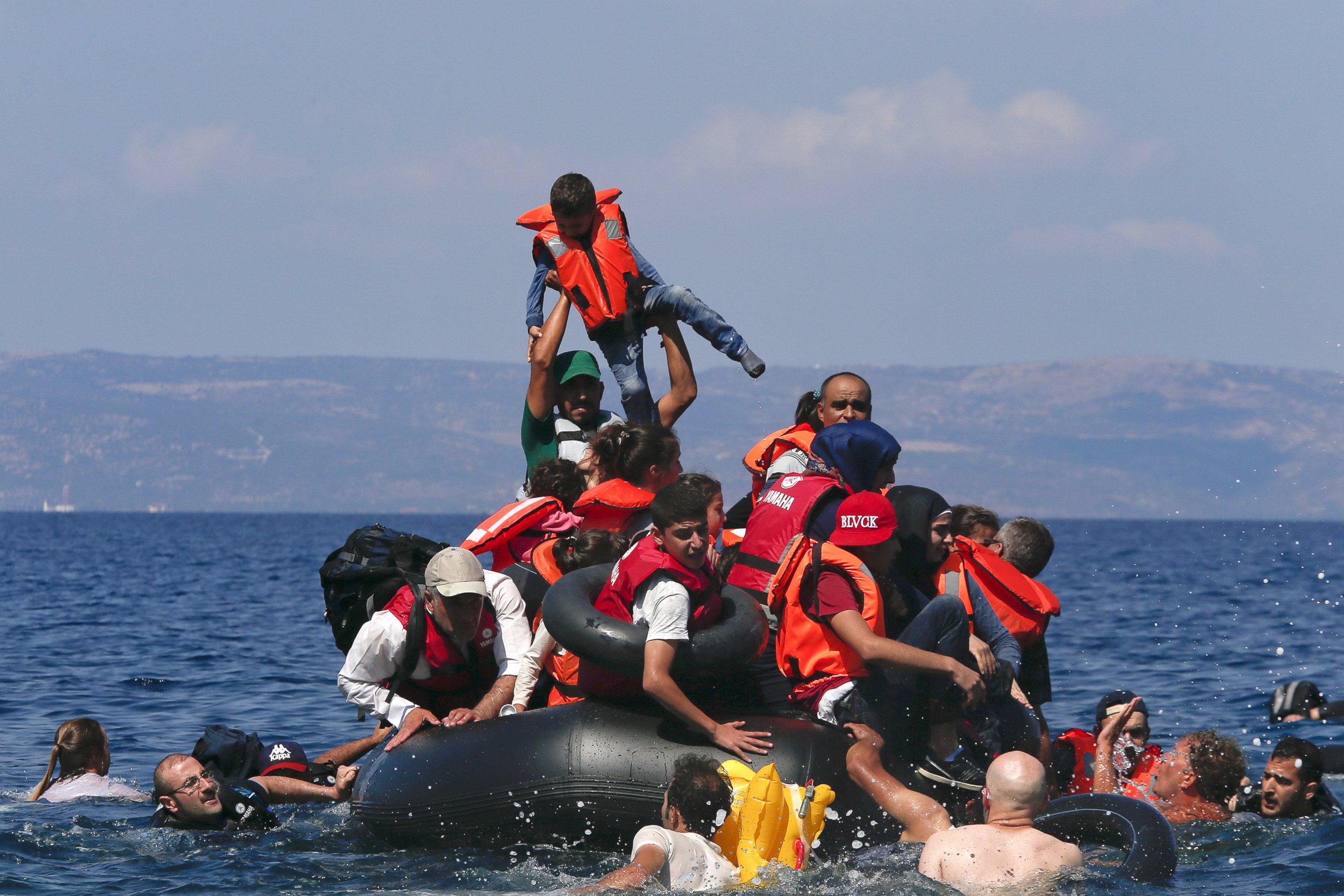 PHOTO: A refugee raises a child into the air as Syrian and Afghan refugees are seen on and around a dinghy that deflated about 100 meters from the Greek island of Lesbos, Sept. 13, 2015.