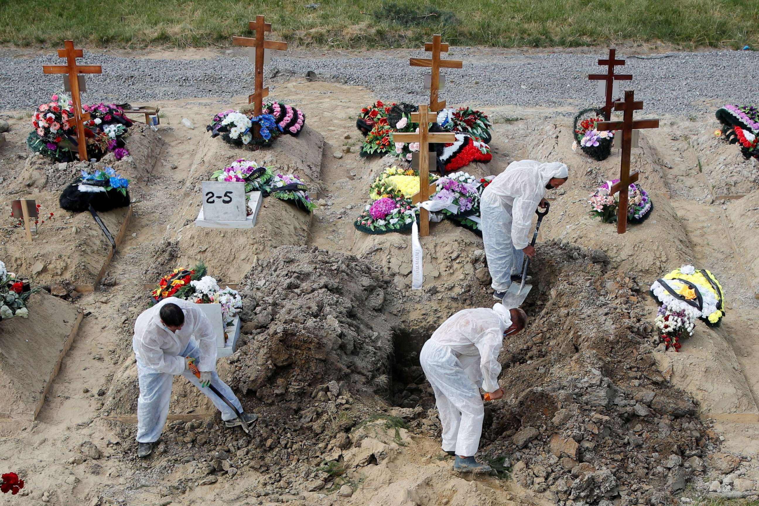 PHOTO: Grave diggers wearing personal protective equipment as a preventive measure against the COVID-19 bury a person at a graveyard on the outskirts of Saint Petersburg, Russia, June 25, 2021. 