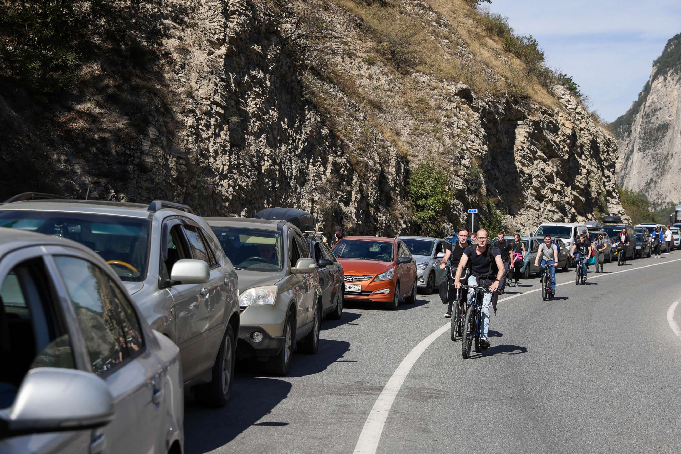 PHOTO: People ride bicycles along a queue of vehicles at the Verkhny Lars checkpoint in North Ossetia, Russia on the border to Georgia, on Sept. 27, 2022. Around 3.5 thousand cars are queueing at the checkpoint to cross the border from Russia to Georgia.