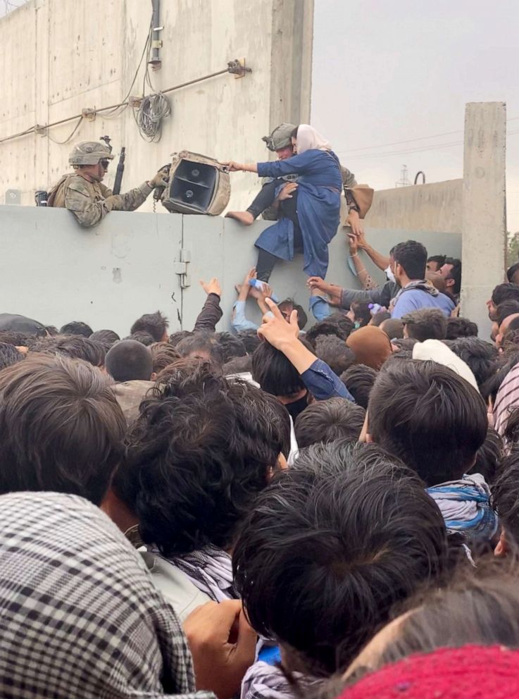 PHOTO: U.S. soldiers help a woman while she tries to climb over a fence as crowds gather near the wall at Kabul airport, Afghanistan Aug 20, 2021, in this still image obtained from social media video.