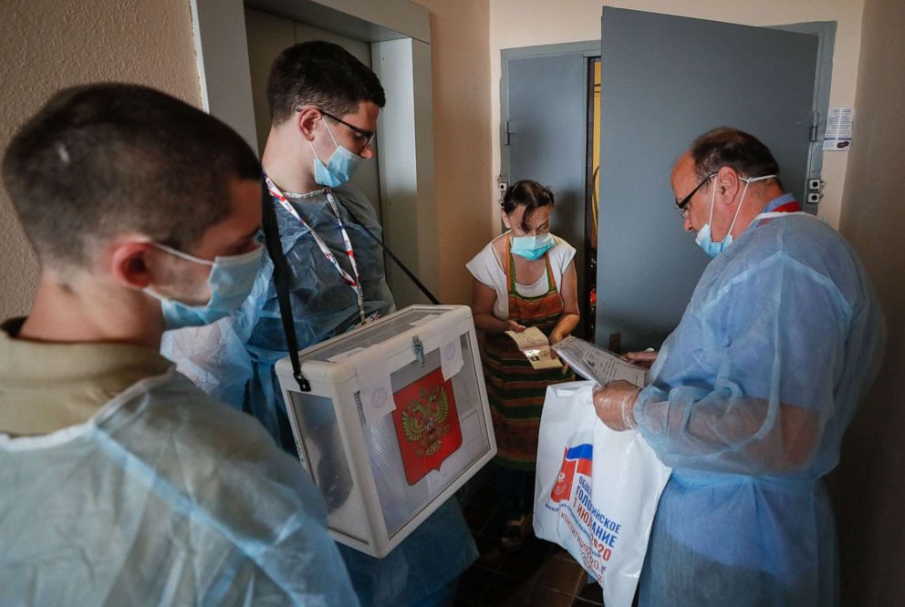 PHOTO: A voter shows her passport to members of a local election commission, wearing protective suits against coronavirus infection, during a nationwide vote on amendments to the Russian Constitution in Moscow, July 1, 2020.