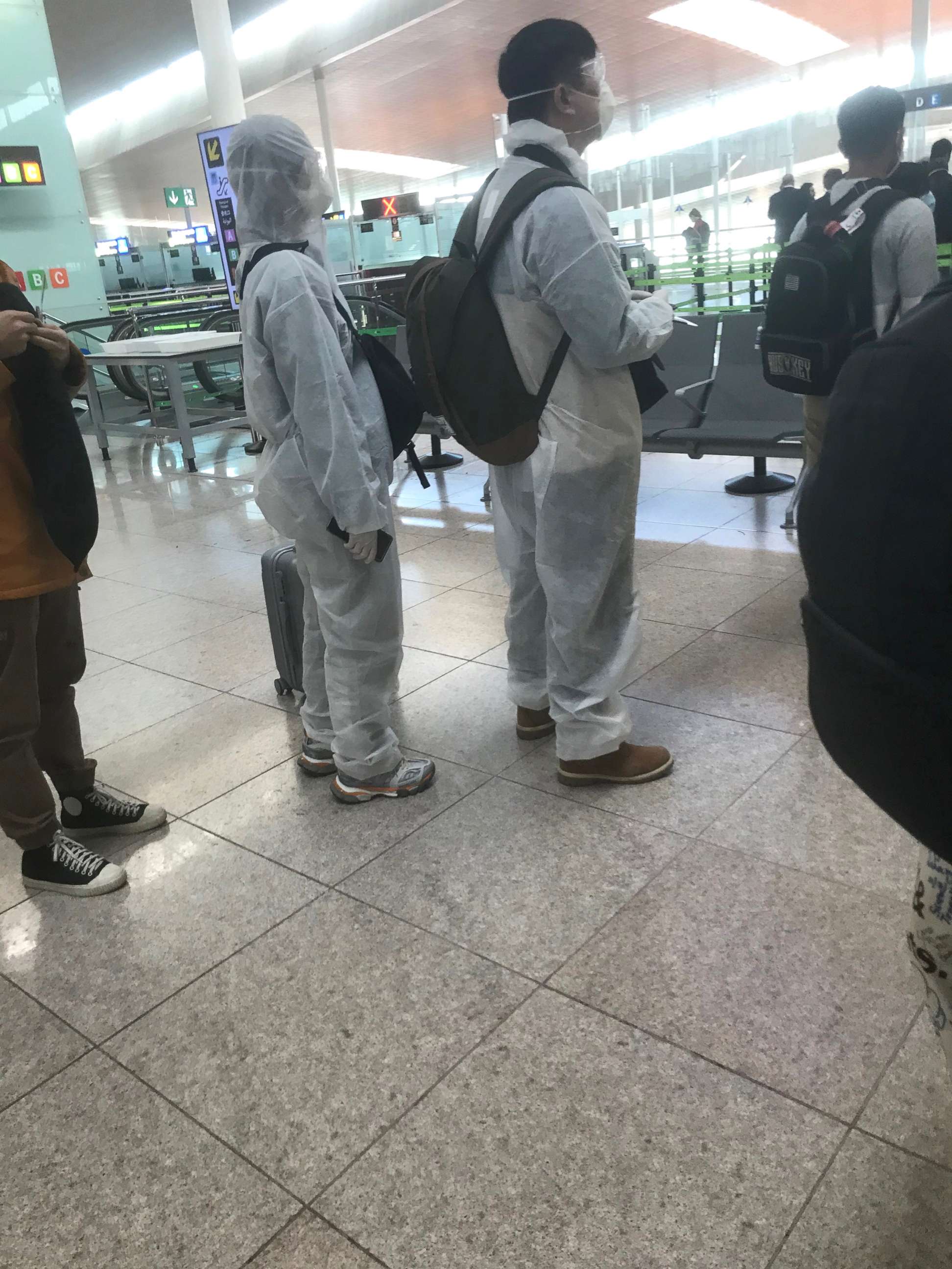 PHOTO: Passengers in the security line wearing hazmat suits at Josep Tarradellas Barcelona-El Prat Airport in Spain.