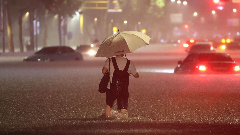 PHOTO: A man wades alongside submerged cars in a street during heavy rainfall in the Gangnam district of Seoul, South Korea, on Aug. 8, 2022.