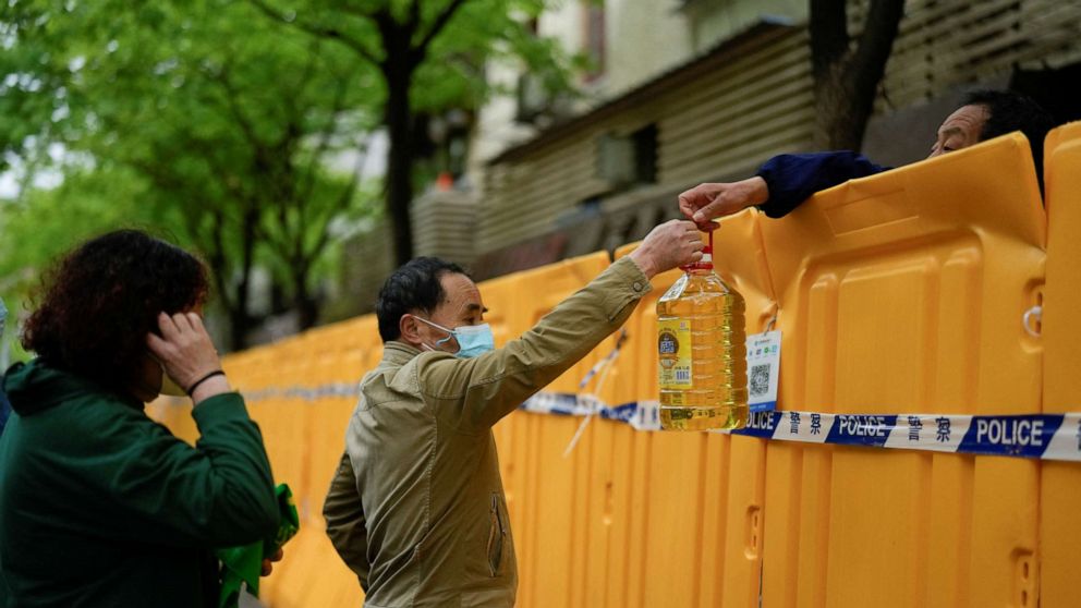 PHOTO: People pass edible oil over the barriers at a street market under lockdown amid the COVID-19 pandemic, in Shanghai, China, April 13, 2022.