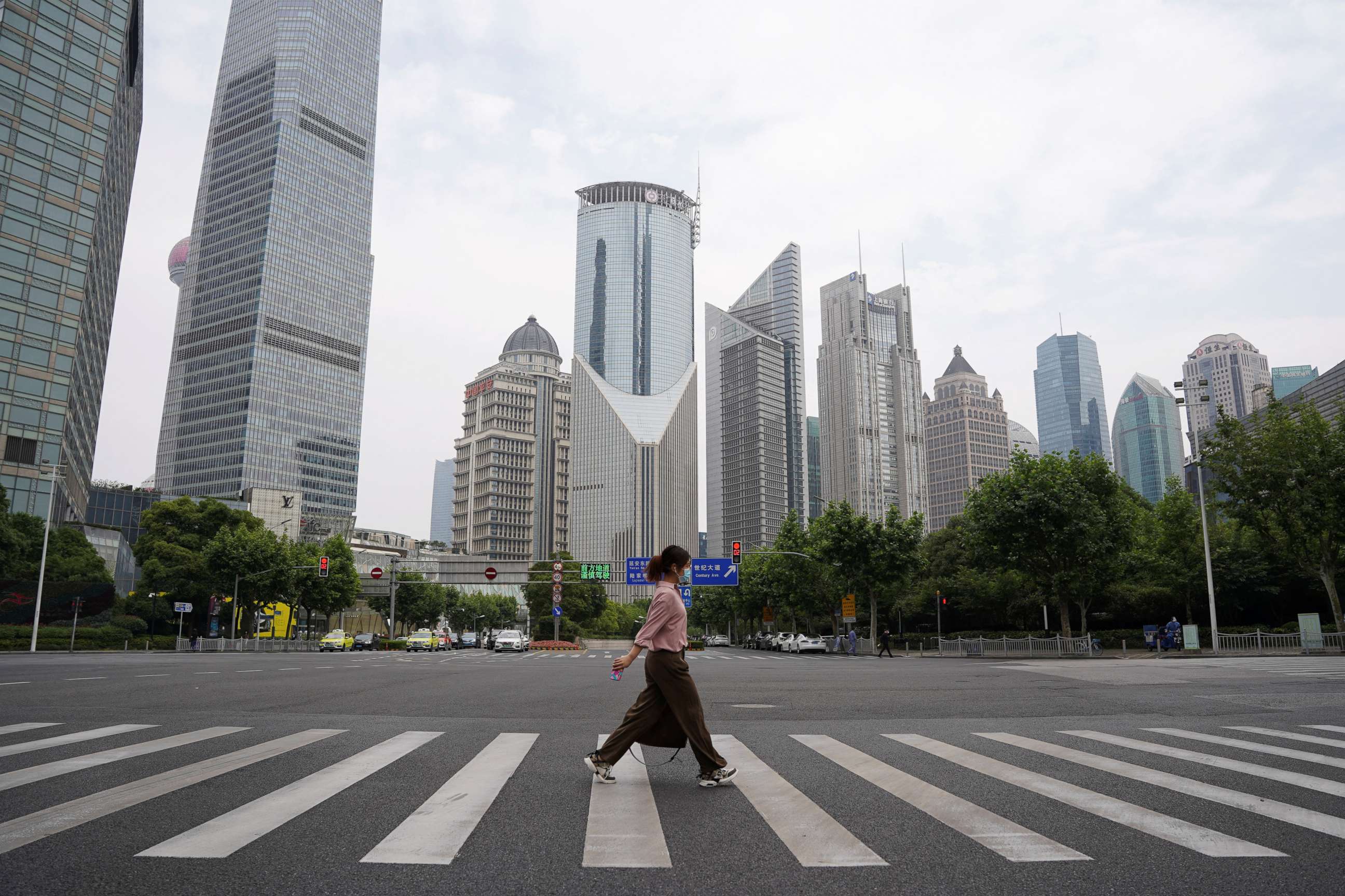 PHOTO: A pedestrian wearing a face mask crosses a road in front of office towers in Lujiazui financial district, after the COVID-19 was lifted in Shanghai, China, June 1, 2022.