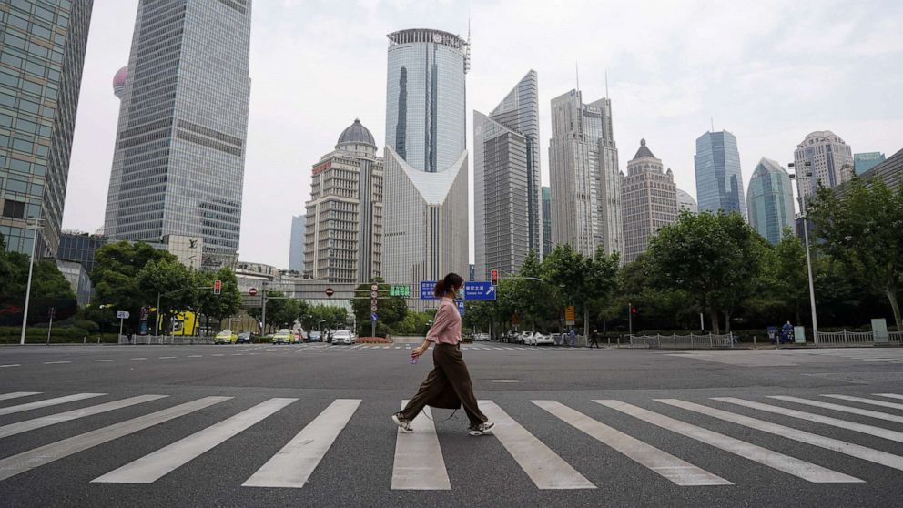 PHOTO: A pedestrian wearing a face mask crosses a road in front of office towers in Lujiazui financial district, after the COVID-19 was lifted in Shanghai, China, June 1, 2022.