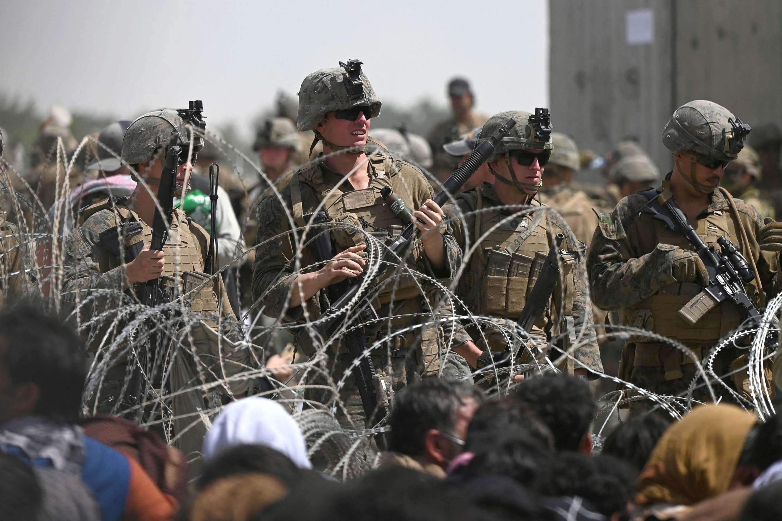 PHOTO: U.S. soldiers stand guard behind barbed wire as Afghans sit on a roadside near the military part of the airport in Kabul, Aug. 20, 2021, hoping to flee from the country after the Taliban's military takeover of Afghanistan.