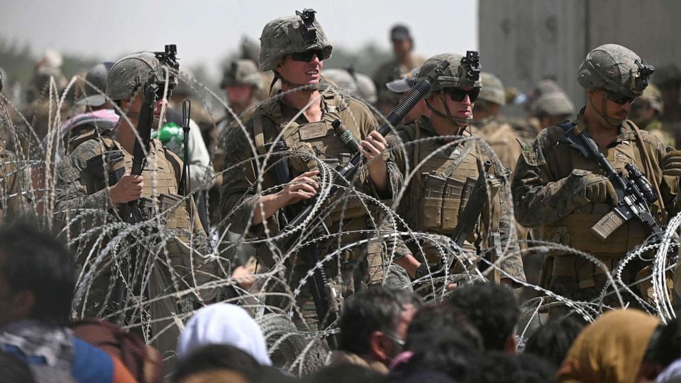 PHOTO: U.S. soldiers stand guard behind barbed wire as Afghans sit on a roadside near the military part of the airport in Kabul, Aug. 20, 2021, hoping to flee from the country after the Taliban's military takeover of Afghanistan.