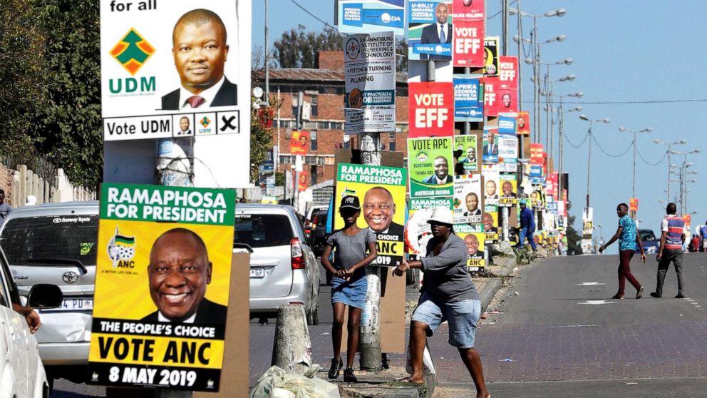 PHOTO: In this May 1, 2019, photo, people walk down a main street adorned with election posters in Alexandra township, South Africa.