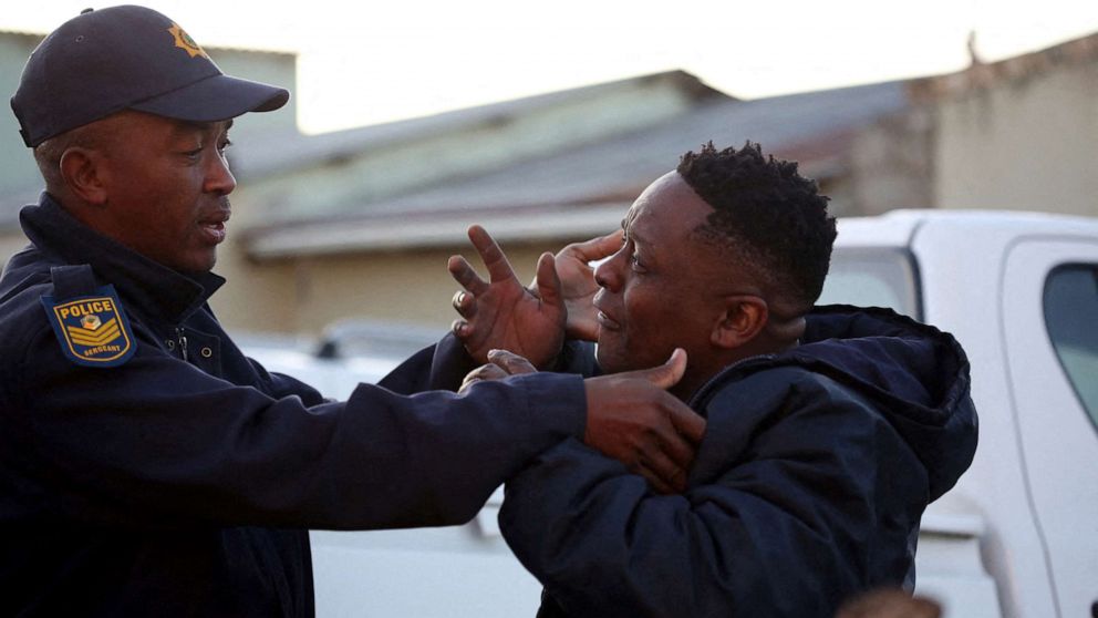 FOTO: Un miembro de la familia reacciona junto a un oficial de policía mientras el equipo forense investiga la muerte de los clientes encontrados dentro de Enyobeni Tavern en Scenery Park en las afueras de East London en la provincia de Eastern Cape de Sudáfrica el 26 de junio de 2022.