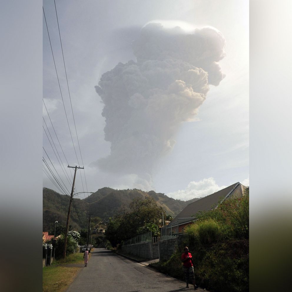 PHOTO: People walk on the side of a road as smoke and ash billow in the background from La Soufriere volcano after it erupted on the eastern Caribbean island of St. Vincent, April 9, 2021.
