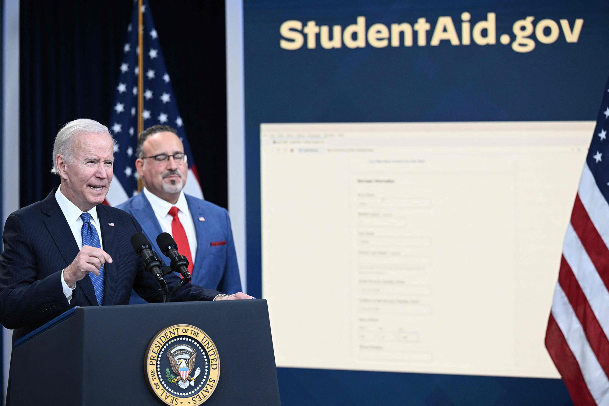 PHOTO: US Education Secretary Miguel Cardona looks on as President Joe Biden delivers remarks on the student debt relief portal beta test, in the South Court Auditorium of the Eisenhower Executive Office Building in Washington, Oct. 17, 2022. 