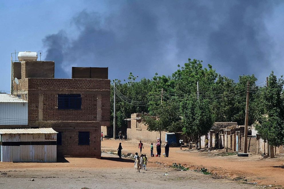 PHOTO: FILE - People walk as smoke billows in the background during fighting in the Sudanese capital Khartoum, May 3, 2023.