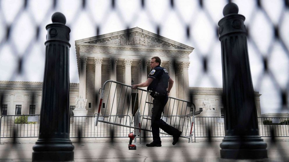 PHOTO: A police officer carrying a barricade is seen through un-scalable fence that stands around the US Supreme Court in Washington, D.C., on May 5, 2022.