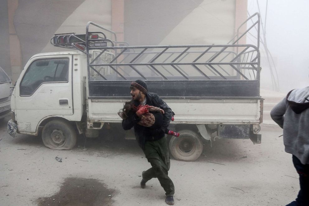 PHOTO: A man carries a child as he flees from reported Syrian air force strikes that hit the rebel-held town of Saqba, in the besieged Eastern Ghouta region outside Damascus, Syria, Feb. 6, 2018.