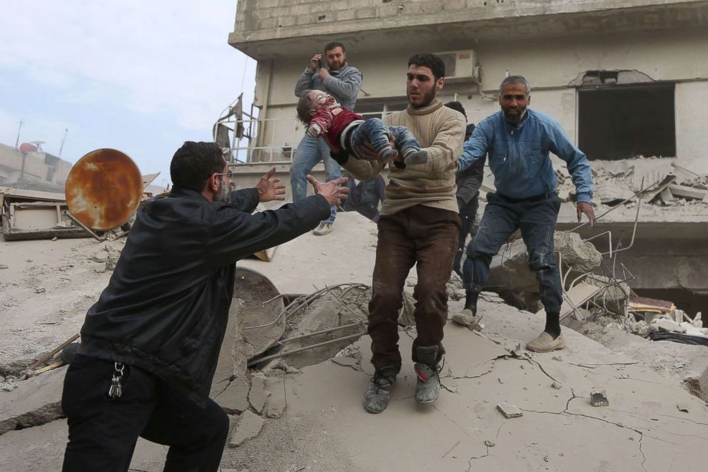 PHOTO: A man passes a child to his father after being rescued from beneath the a building that collapsed following reported Syrian air force strikes in the rebel-held town of Saqba, in the Eastern Ghouta region, outside Damascus, Feb. 6, 2018.