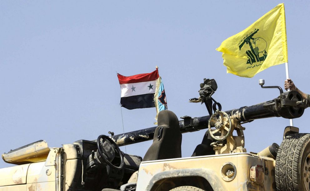 PHOTO: A picture taken on August 2, 2017 during a tour guided by the Lebanese Shiite Hezbollah movement shows the flags of the movement (R) and the Syrian national flag (L) flying at a position in Syria near the border with Lebanon.