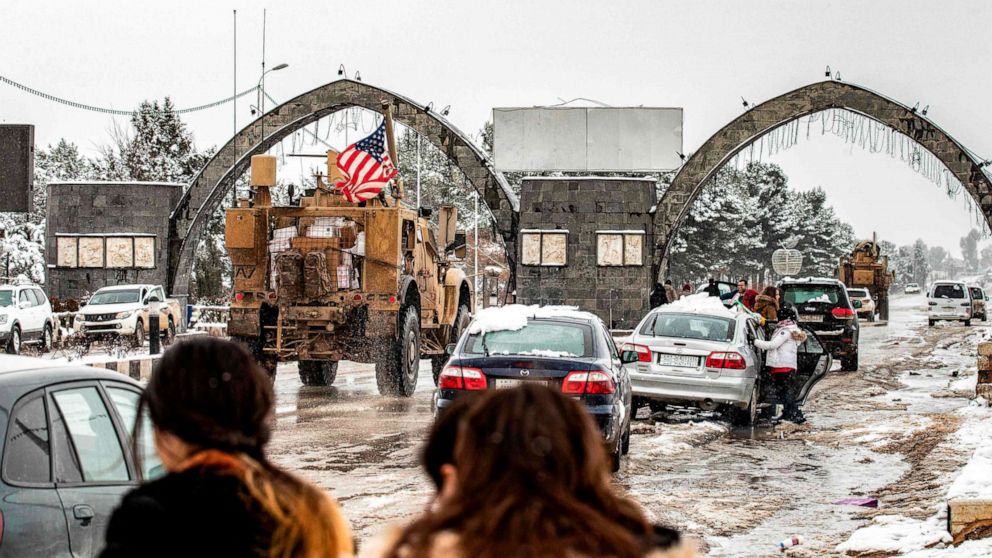 PHOTO: People look at a U.S. military patrol passing by other cars in the snow-covered northeastern Syrian town of al-Malikiyah at the border with Turkey on Feb. 10, 2020.