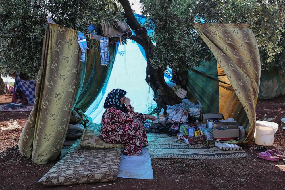 PHOTO: A displaced Syrian woman sits under the shade of a tree in a field near a camp for displaced people in the village of Atme, May 19, 2019.