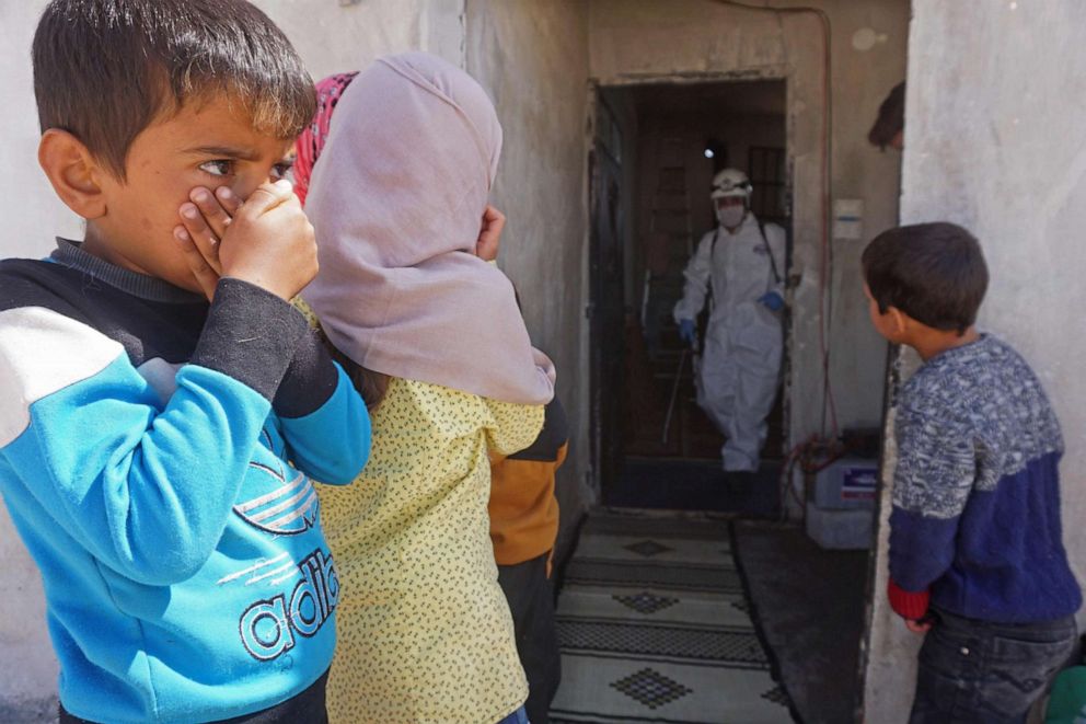 PHOTO: Syrian children watch a member of the Syrian Civil Defence, known as the White Helmets, disinfecting a former school building currently inhabited by displaced families in the rebel-held town of Binnish in northwestern Syria on March 26, 2020.