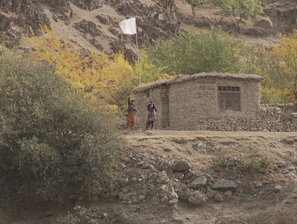 PHOTO: Two men wave after emerging from a hut with a Taliban flag flying on the Afghan side of the border.