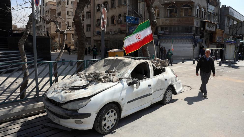 PHOTO: A man walks past an Iranian flag fluttering above the wreckage of a car in central Tehran, on March 4, 2026. 