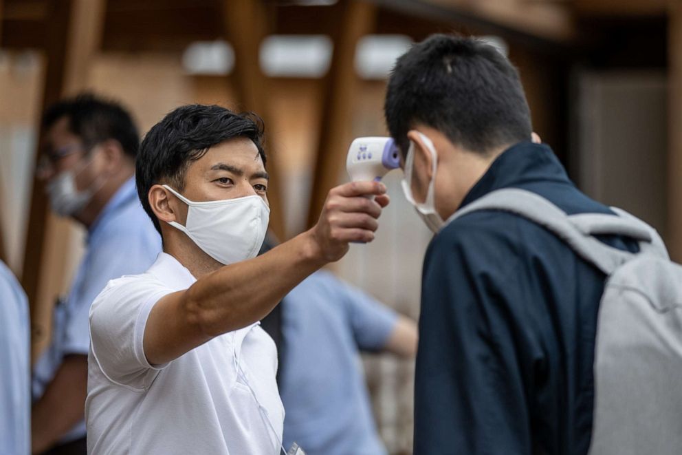 PHOTO: An employee checks the body temperature of a man during a press preview of the Village Plaza as part of a media tour of the Tokyo 2020 Olympic and Paralympic Village in Tokyo, Japan, on June 20, 2021.