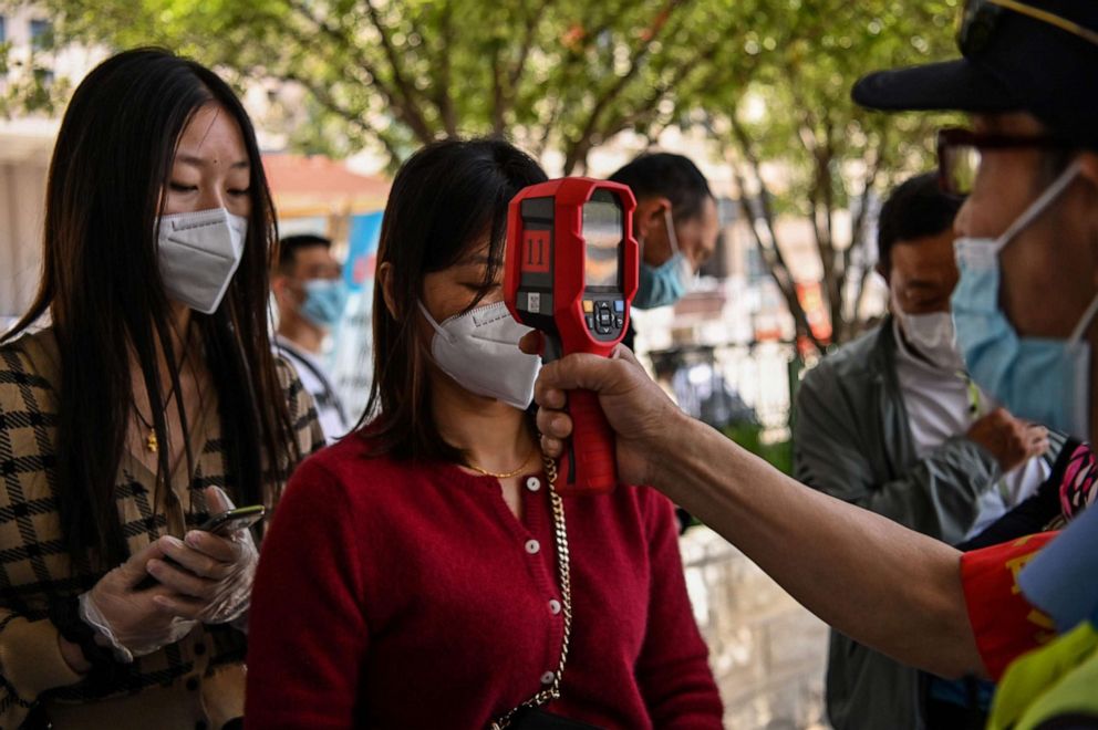 PHOTO: A worker wearing a face mask checks passengers' body temperatures as well as a health code on their cellphones before they take a taxi after arriving at Hankou railway station in Wuhan, in China's central Hubei province, on May 12, 2020.