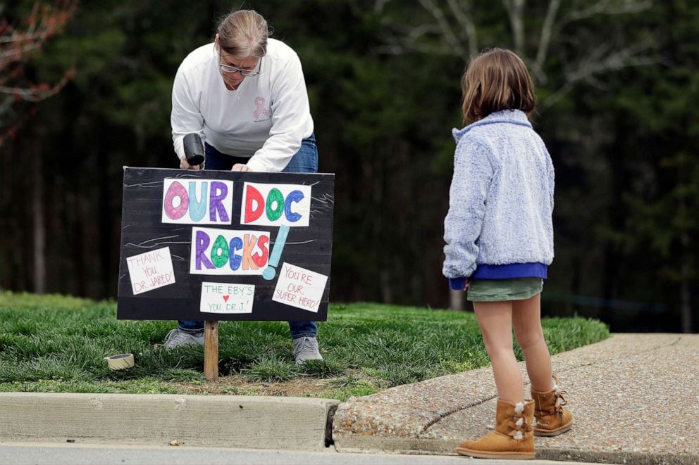 PHOTO: Andrea Eby, left, puts up a yard sign showing support for a doctor who is a neighbor, March 22, 2020, in Nolensville, Tenn.