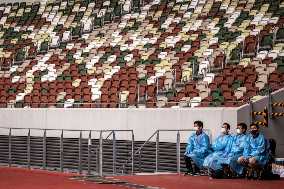 PHOTO: Staff members wearing face masks and protective clothing sit near empty seats during a para-athletics test event for the 2020 Tokyo Olympics at the National Stadium in Tokyo, Japan, on May 11, 2021.