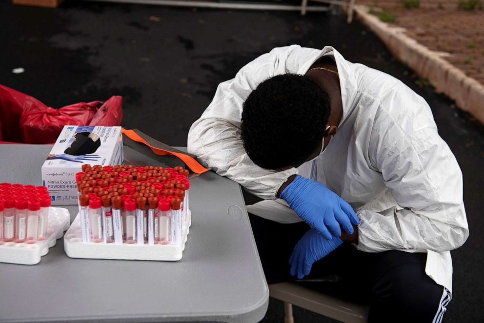 PHOTO: A healthcare worker takes a break as people wait in their vehicles in long lines in the heat for COVID-19 testing in Houston, July 7, 2020.