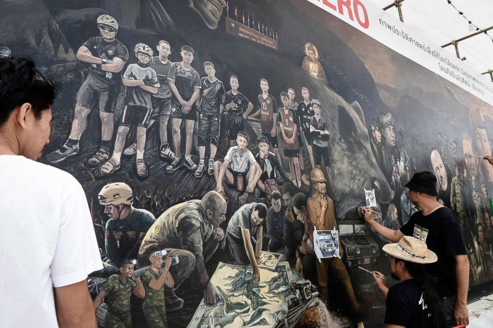 PHOTO: Local artists work on a mural dedicated to the successful rescue of the Wild Boars football team outside an art gallery in Chiang Rai province, July 18, 2018, as family members await for the childrens homecoming.