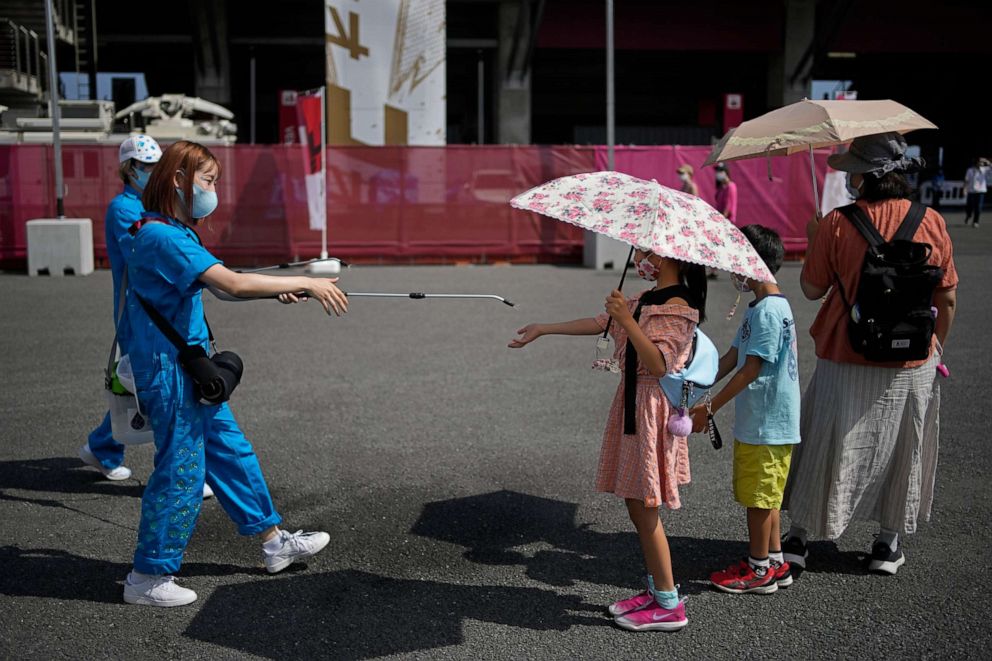 PHOTO: A volunteer sprays water on children as they use umbrellas to beat the heat outside the Fuji International Speedway at the 2020 Summer Olympics, July 25, 2021, in Oyama, Japan.