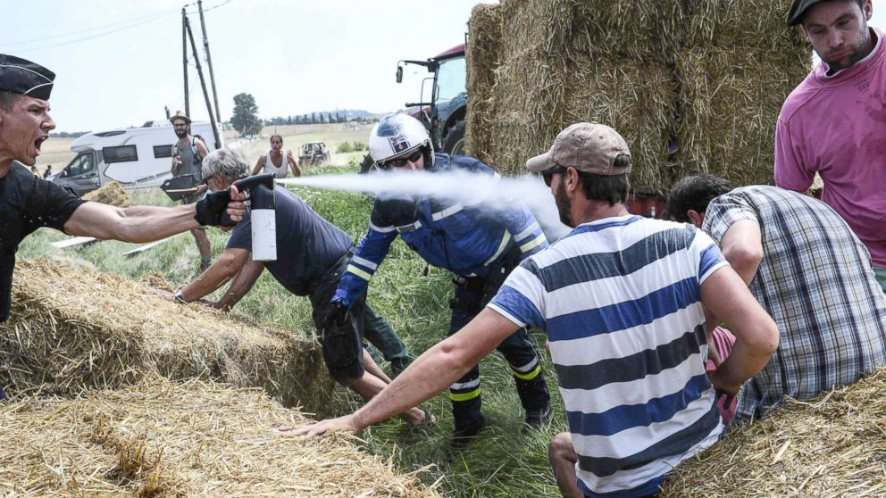 A gendarme (L) sprays tear gas at protesters as other gendarmes remove haystacks from the route, during a farmers' protest who attempted to block the stage's route, during the 16th stage of the 105th edition of the Tour de France cycling race, between Carcassonne and Bagneres-de-Luchon, southwestern France, on July 24, 2018.