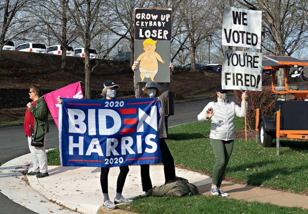 PHOTO: Demonstrators holding signs that read 'We voted you're fired!' and 'Grow up crybaby loser' rally at Trump National Golf Club as the motorcade carrying President Donald Trump arrives., in Sterling, Va., Nov. 14, 2020.