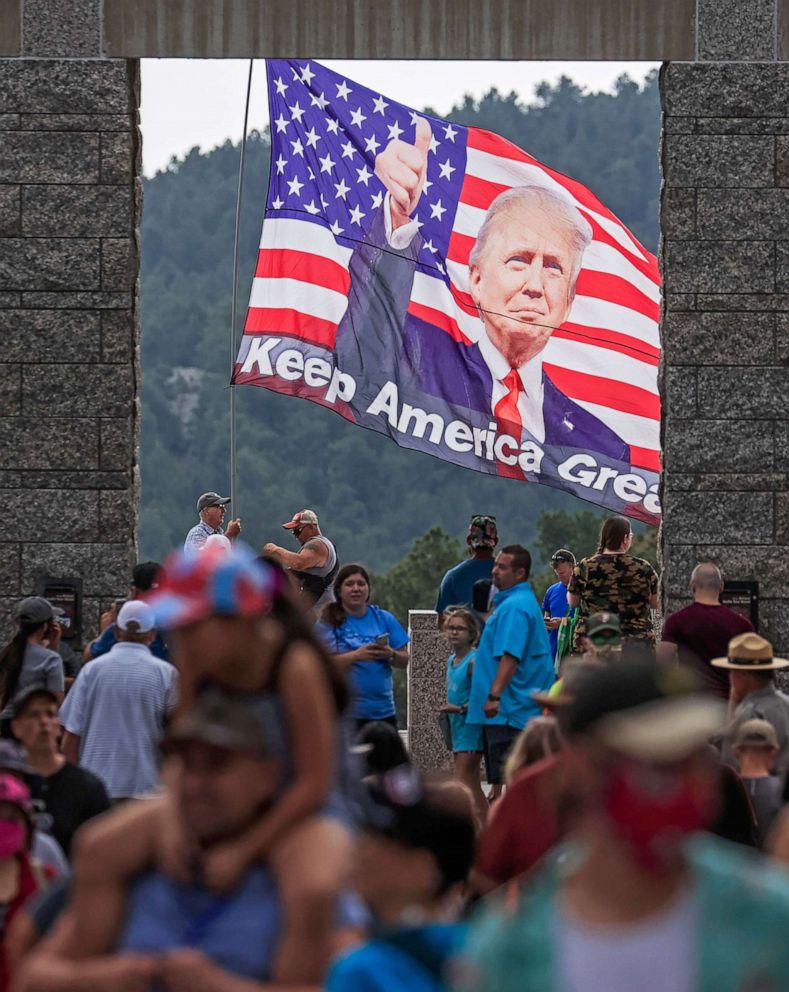 PHOTO: Visitors walk on the grounds as a man waves a flag supporting President Donald Trump at the Mt. Rushmore National Monument in Keystone, South Dakota, July 2, 2020.